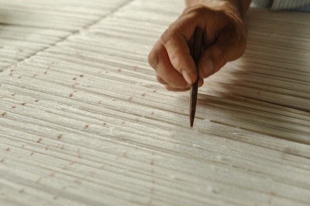 Hand met een potlood maakt markeringen op het tapijt Weven en vervaardigen van handgemaakte tapijten close-up