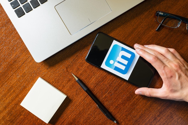 Hand met een smartphone met de linkedin-applicatie op een bureau