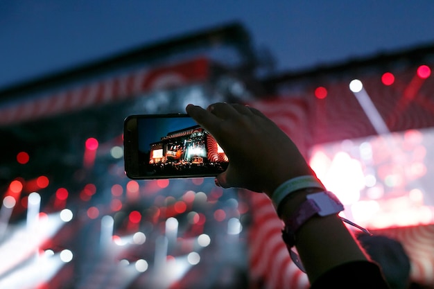 Hand met een smartphone neemt live muziekfestival op en maakt foto van concertpodium