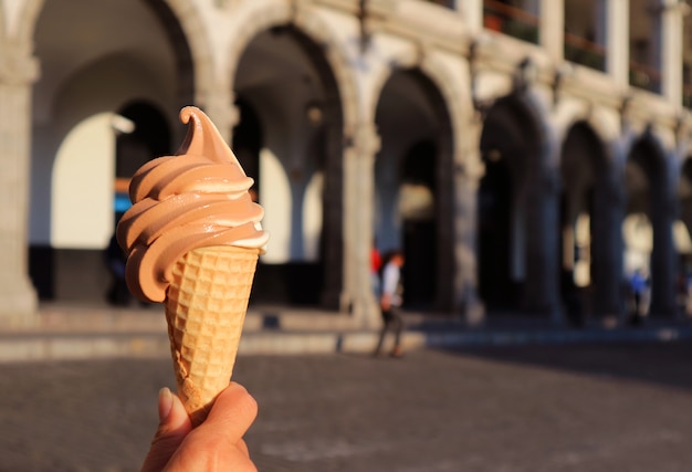 Hand met een tweekleurige soft-serve ijsje, met wazig neoklassiek gebouw