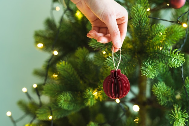 Hand met gekleurde papieren ballen voor kerstversiering met verlichting en boomachtergrond Kopieer de ruimte