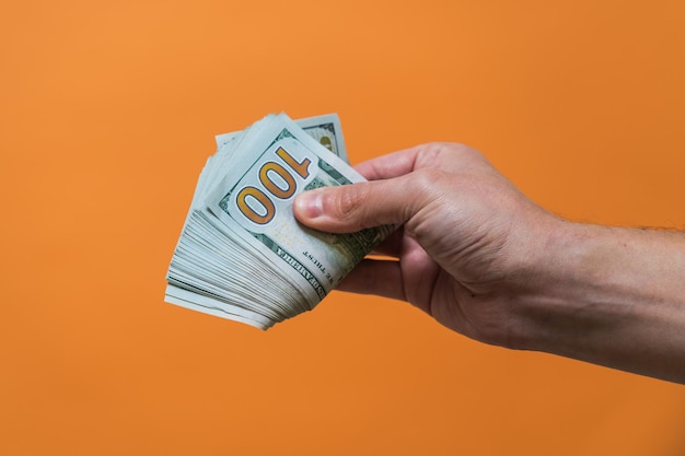 Hand met geld op oranje achtergrond Amerikaanse dollars Geld of bedrijfsconcept