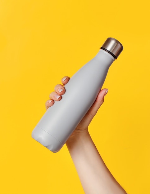 Hand met grijze herbruikbare geïsoleerde fles op gele achtergrond. Zero waste, plasticvrij en duurzaam levensstijlconcept