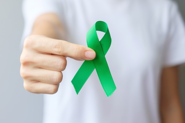 Hand met groen lint voor lever, galblaas, galwegen, baarmoederhalskanker, nierkanker en lymfoom Awareness maand. Gezondheidszorg en wereldkankerdagconcept