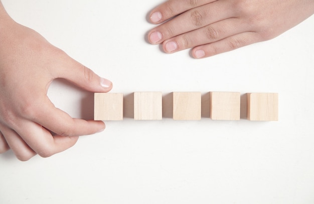 Hand met houten kubus op een wit bureau.