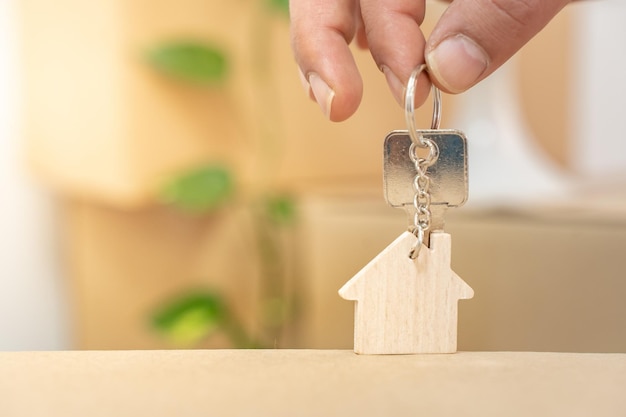 Hand met huissleutels aan sleutelhanger in de vorm van een houten huis met copyspace voor tekst