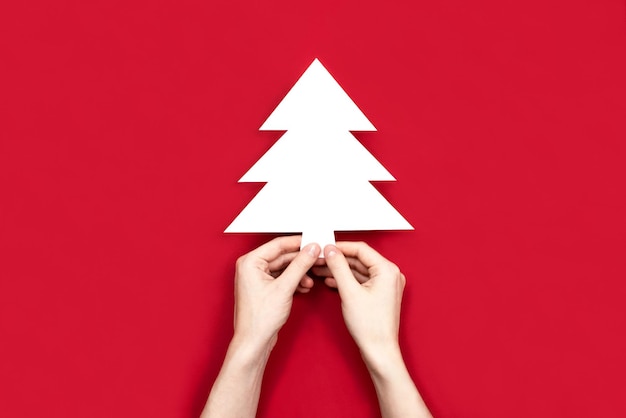 Hand met kerst dennenboom silhouet gesneden uit wit papier plat lag kopie ruimte rode achtergrond
