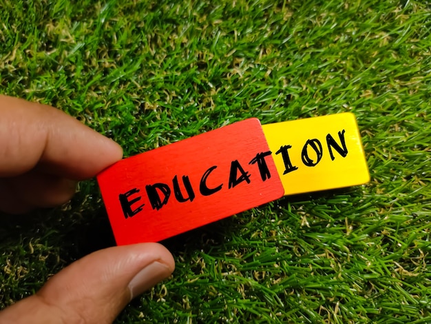 Foto hand met kleurrijke houten plank met tekst onderwijs op groen gras achtergrond