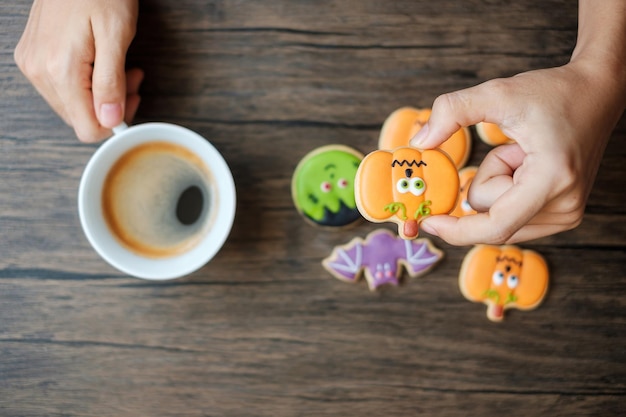 Hand met koffiekopje tijdens het eten van grappige Halloween-koekjes Happy Halloween-dag Trick or Threat Hallo oktober herfst herfst Traditioneel feest en vakantieconcept