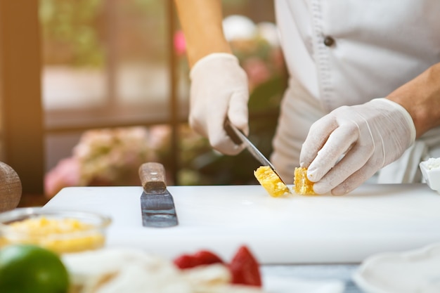 Hand met mes snijdt honingraat. Honingraat op kookbord. Natuurlijk ingrediënt voor het dessert. Decoratie voor honingcake.