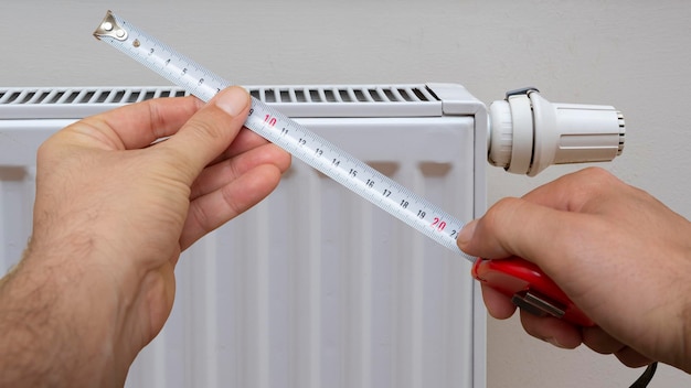 Hand met meter op moderne witte radiator met thermostaat