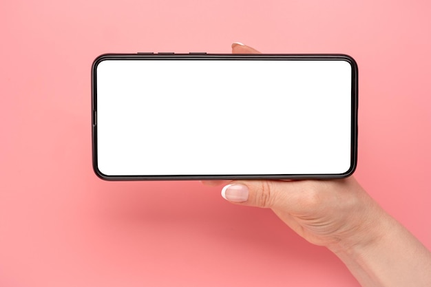 Hand met mobiele telefoon in horizontale positie voor mockup kijken naar streaming video op mobiele telefoon op roze tafelachtergrond close-up vrouw handen houden mobiele telefoon