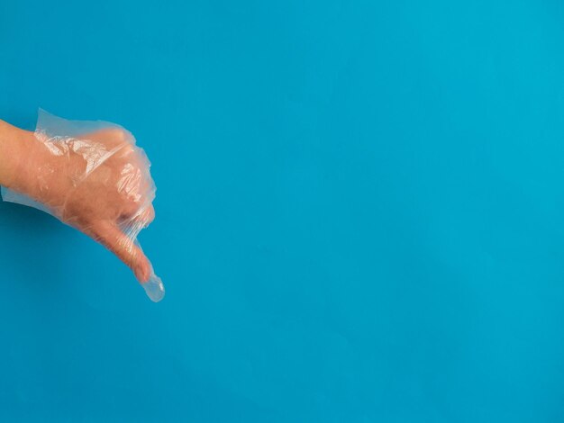 Foto hand met plastic handschoen met duim naar beneden op blauwe achtergrond met kopieerruimte