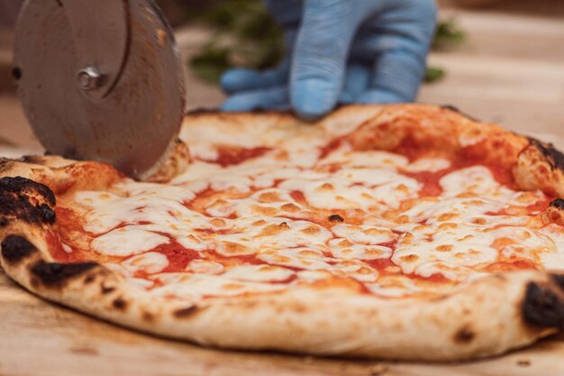 Foto hand met plastic handschoen snijdt hete pizza margherita met tomatensaus en mozzarella met een cutter