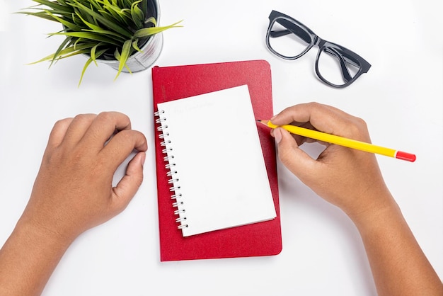 Hand met potlood schrijven in notitieboek op wit bureau