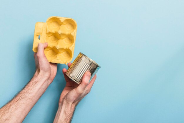 Hand met recyclingafval tegen een blauwe achtergrond