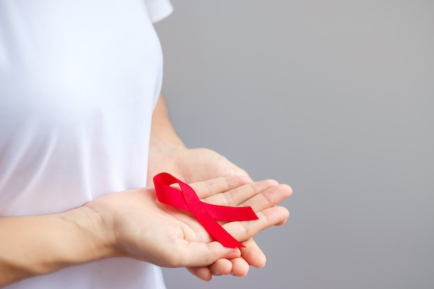 Hand met Red Ribbon voor december Wereld Aids Dag (acquired immune deficiency syndrome), multipel myeloom Cancer Awareness Month en National Red Ribbon Week. Gezondheidszorg en wereldkankerdagconcept