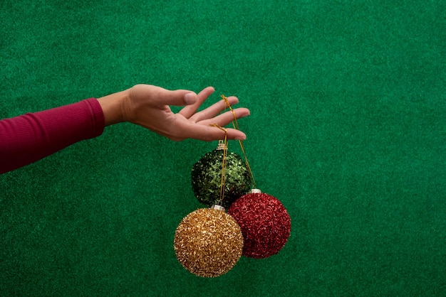 Hand met rode, groene en gouden kerstballen op een glanzende groene achtergrond