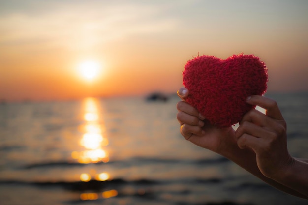 Hand met rood handwerkhart aan zee bij avondzonsondergang