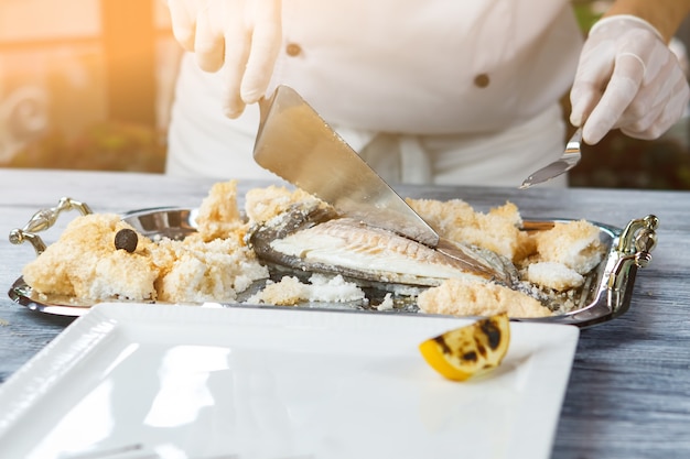 Hand met spatel die vis snijdt. Dienblad met gekookte vis. Dorado vis bereid door chef-kok. Zeevruchten delicatesse in de keuken van het restaurant.