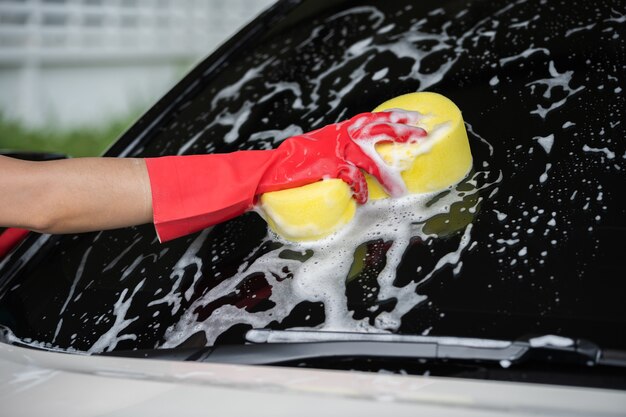 Hand met spons aan het wassen van het venster van de auto