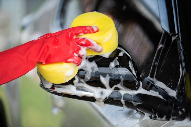 Hand met spons wassen zijspiegels van een auto