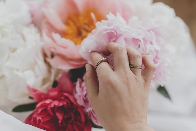 Hand met stijlvolle ringen aan prachtig pioenrozenboeket tedere afbeelding vrouwelijke essentials
