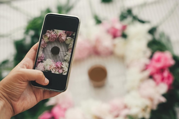 Hand met telefoon en het nemen van foto's van koffie drinken in prachtige roze en witte pioenrozen frame op tafel plat leggen Goedemorgen concept Gelukkige moederdag Instagram bloggen en workshop