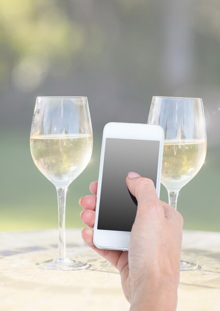 Hand met telefoon met twee glazen champagne en zonnig groen