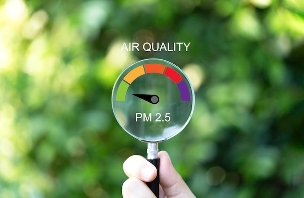 Foto hand met vergrootglas met goede luchtkwaliteitsindicatorschaal op groene achtergrond die pm 25 of fijnstof 25 micron controleert op luchtverontreinigingseffect op het gezondheids- en levensstijlconcept