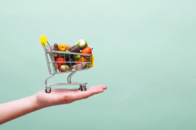 Hand met winkelwagentje met groenten en fruit op blauwe achtergrond Voedsel levering concept