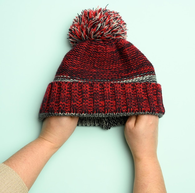 Foto hand met winter gebreide rood-zwarte hoed met pompon op een groene achtergrond comfortabele kleding