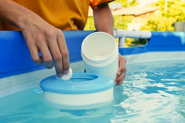 Hand met witte chloortabletten boven zwembad skimmer chlorering van water in zwembad voor dis ...