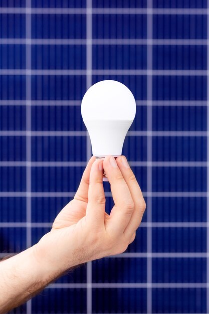 Hand met witte lamp tegen zonnepaneel, zonnestation. Idee concept van alternatieve energie, technologie, milieu, ecologie. Groene stroom energie.