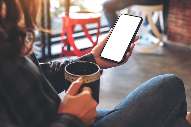 hand met zwarte mobiele telefoon met leeg scherm terwijl het drinken van koffie in café