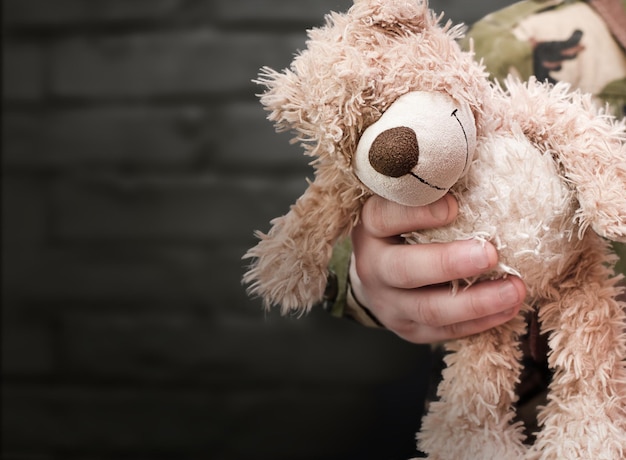 The hand of a military man holds out a teddy bear