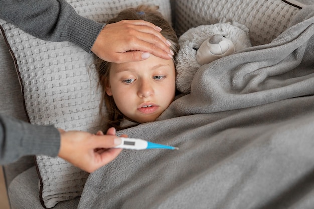 Hand of millennial caucasian woman touches forehead and checks temperature on thermometer
