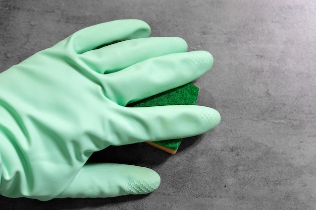 Рука в мятно-зеленой резиновой перчатке вытирает оранжевой губкой мокрую серую кафельную бетонную стену.