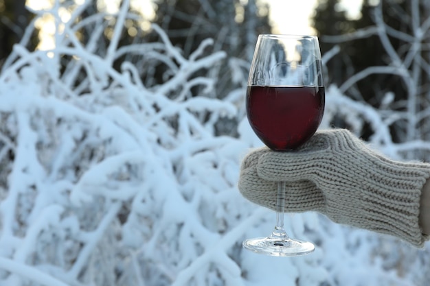 Hand in mitten holds glass of wine in forest