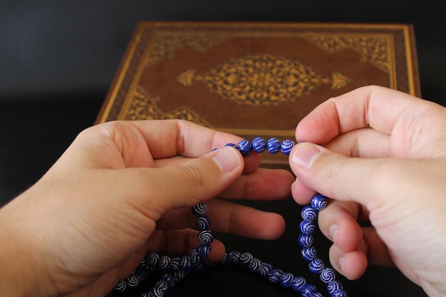 hand of muslim praying with rosary on quran background