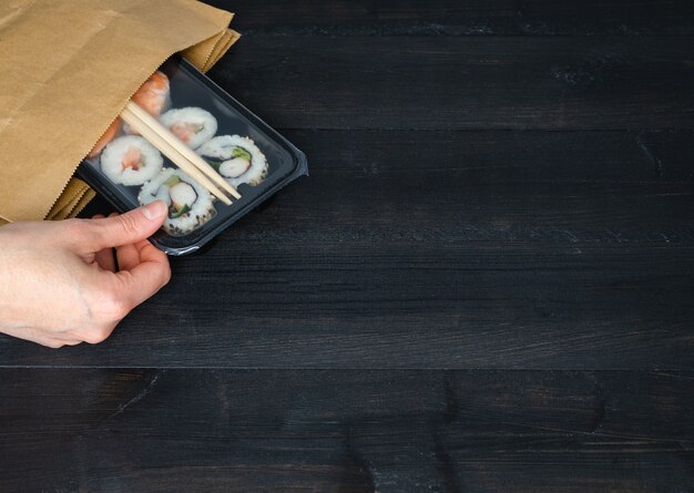 Hand nemend sushi lade uit papieren zak op zwarte houten achtergrond. Kopieer ruimte. Voedsel concept.