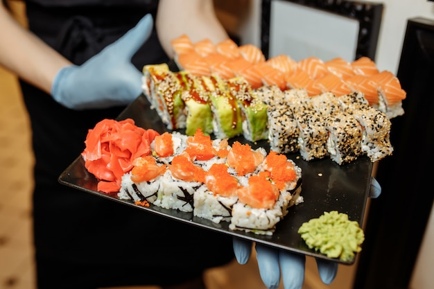 Hand ober bedrijf Set Heerlijke verse Sushi leisteen plaat, Japanse rauwe vis in traditioneel restaurant. Philadelphia verse broodjes geserveerd op plaat in sushibar. ober in handschoenen houdt sushibroodjes.