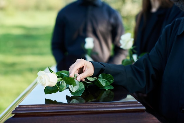 Фото Рука зрелой женщины в траурном наряде кладет белую розу на крышку гроба