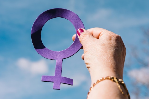 Hand of an older woman with purple nails with the sky in the background holding the female symbol in purple Concept of women39s day empowerment equality inequality activism and protest