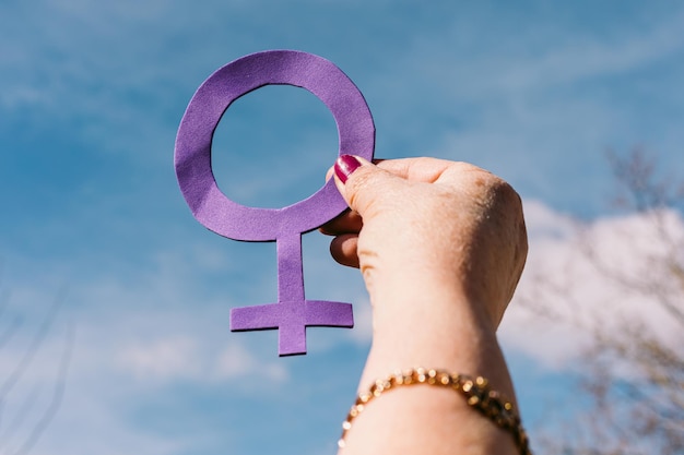 Hand of an older woman with purple nails with the sky in the
background holding the female symbol in purple concept of women39s
day empowerment equality inequality activism and protest