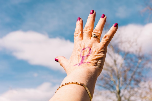 Hand of an older woman with purple painted nails with the sky
in the background with the female symbol painted purple concept of
women39s day empowerment equality inequality activism and
protest