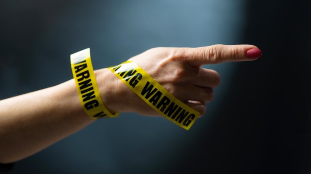 Hand omwikkeld met gele waarschuwingstape met waarschuwingswoorden toont richting met vinger