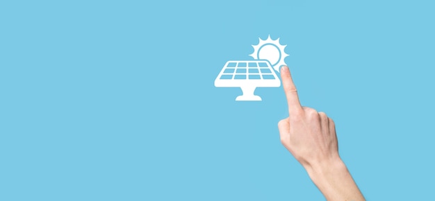 Hand op een blauwe achtergrond houdt het pictogramsymbool van zonnepanelen vast. Hernieuwbare energie, zonnepanelen station concept, groene stroom.