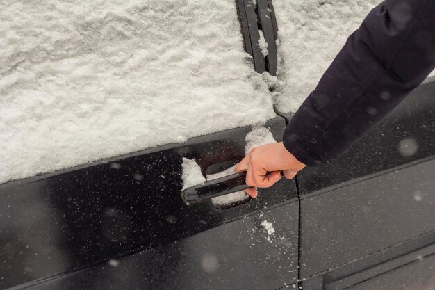 Hand op het handvat van de auto Close-up van de hand van een man die de deur van een besneeuwde auto opent