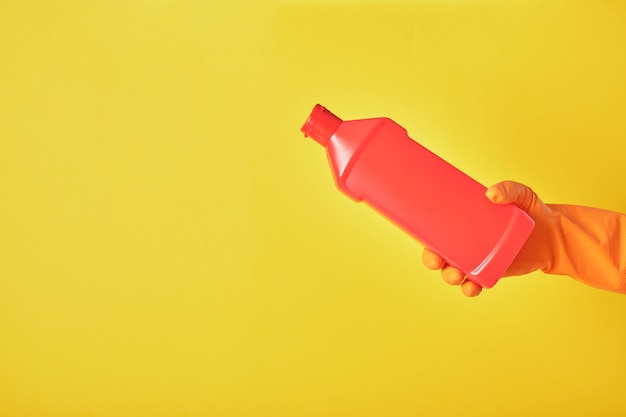 hand op rubberen handschoen houdt rode fles met wasgel zonder label op gele achtergrond
